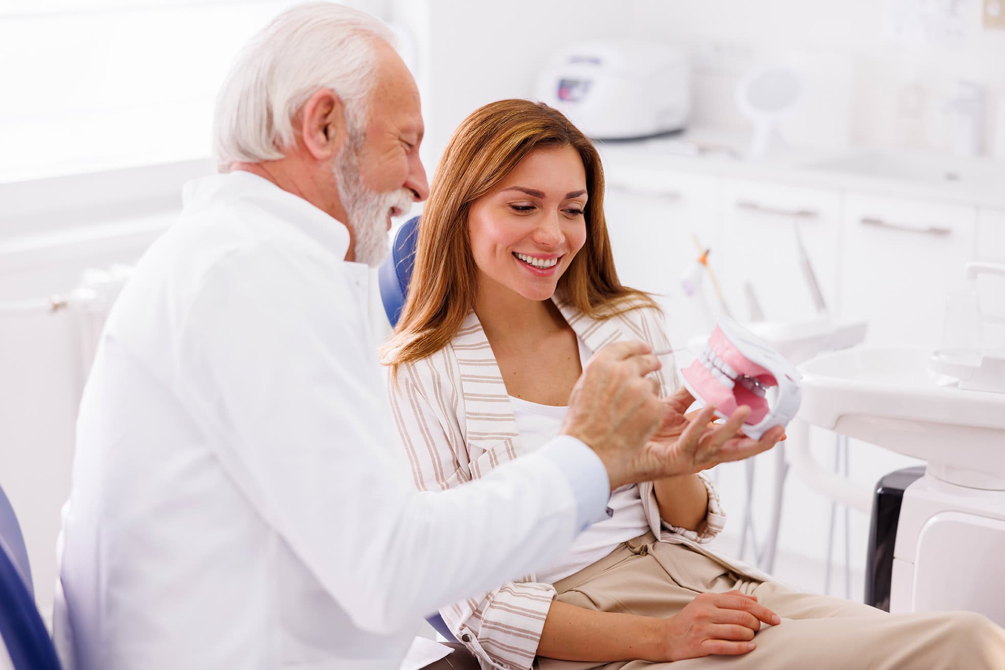 Dentist holding plastic jaw model and explaining necessary medical procedure to patient in dental clinic